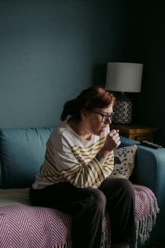 Woman sitting on a couch and coughing.