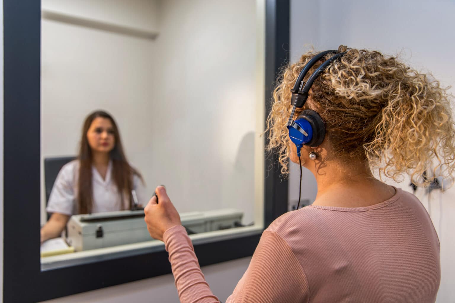 Woman takes a hearing test inside of an audiology booth.