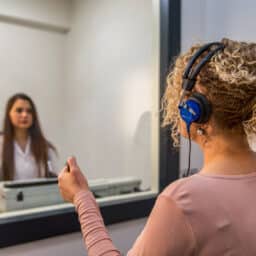 Woman takes a hearing test inside of an audiology booth.