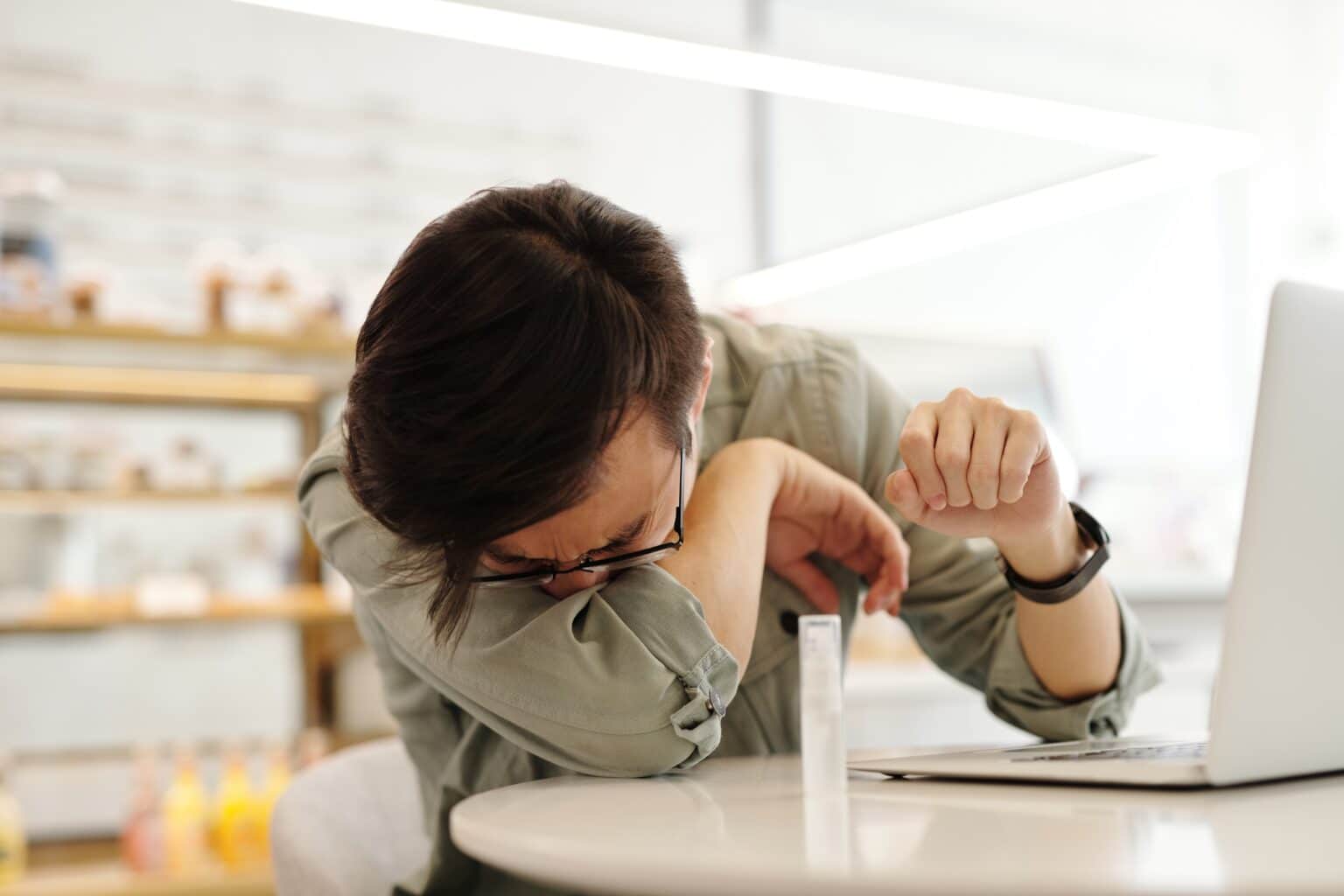 Man sneezing into his elbow at an indoor coffee shop.