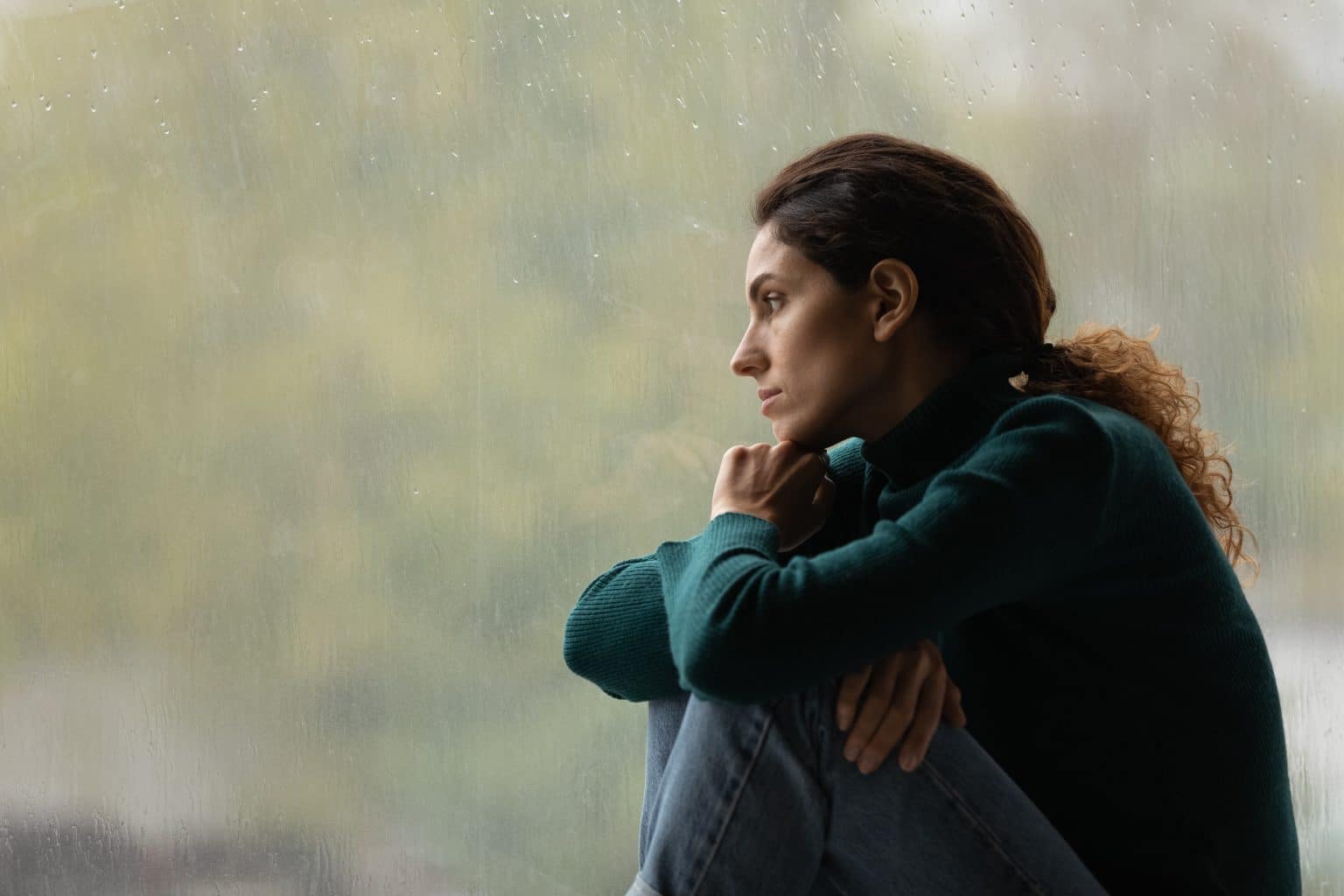 A woman with a sad expression looks out of a window