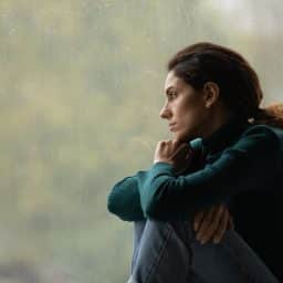 A woman with a sad expression looks out of a window