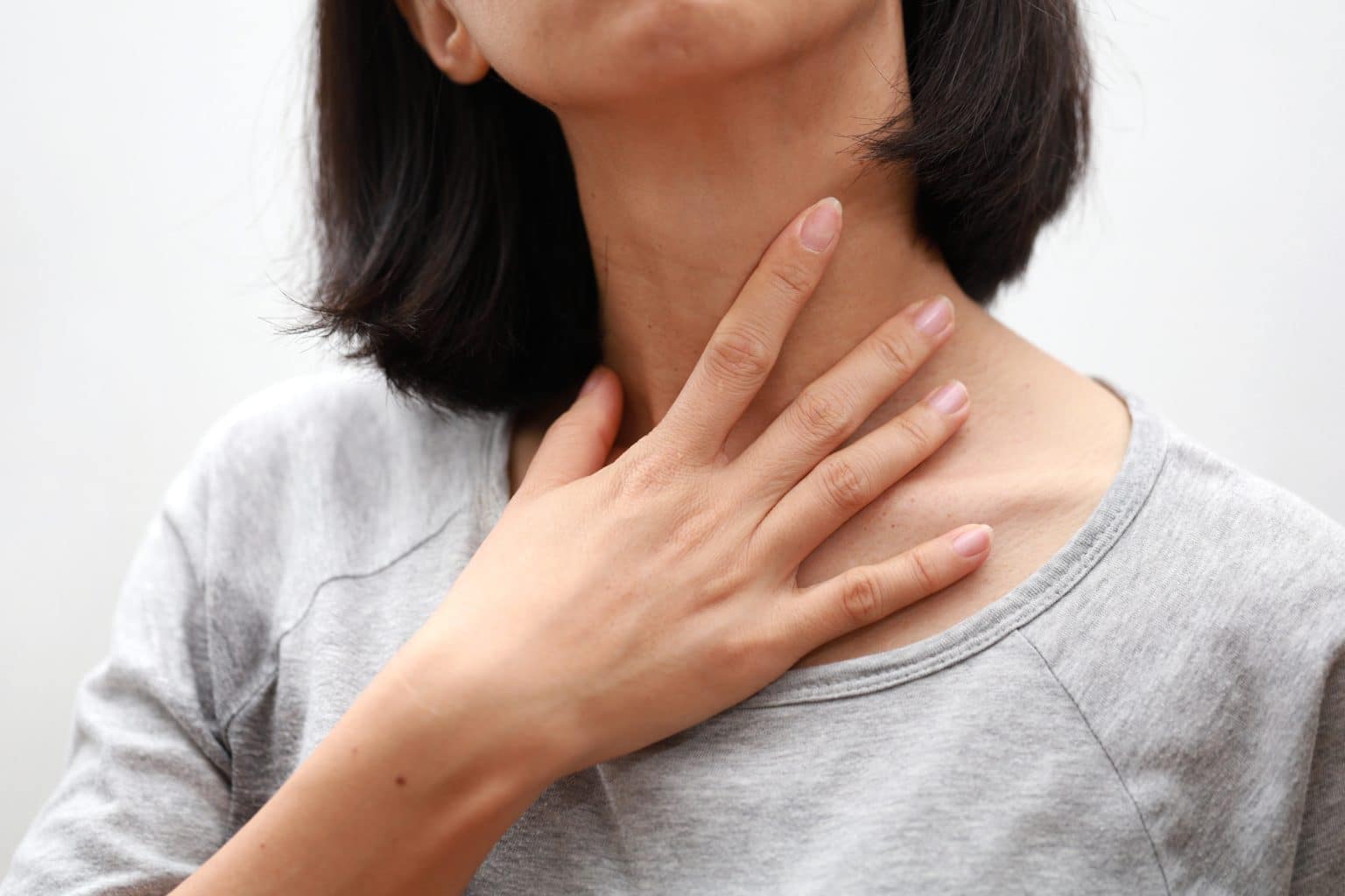 Close up of a woman reaching to touch her sore throat.