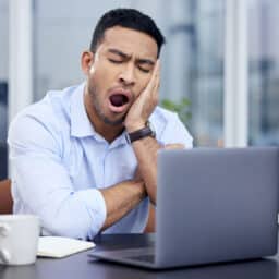 Young businessman yawning while looking at his computer.