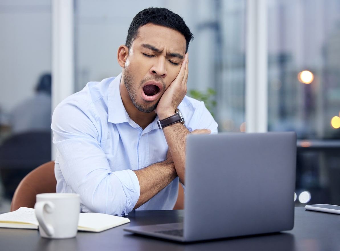 Young businessman yawning while looking at his computer.
