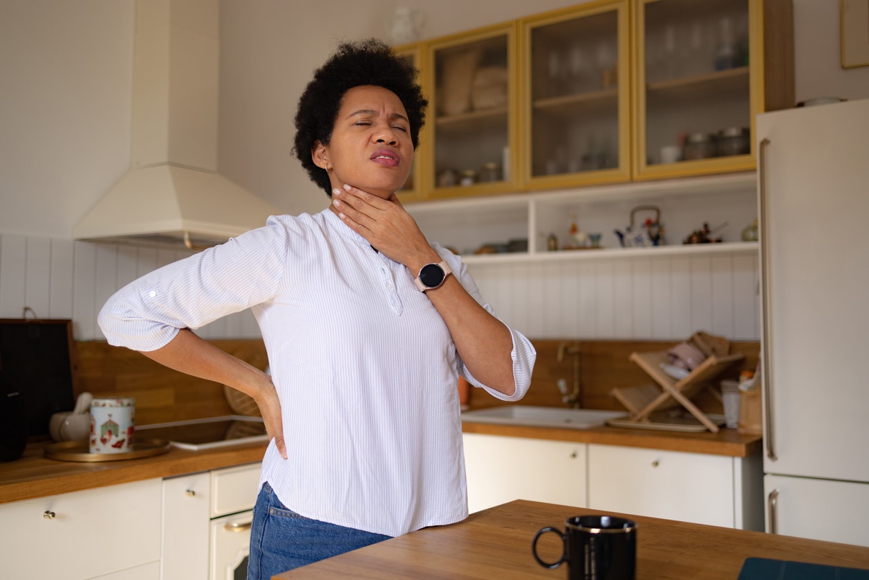Woman at home holding her sore throat.