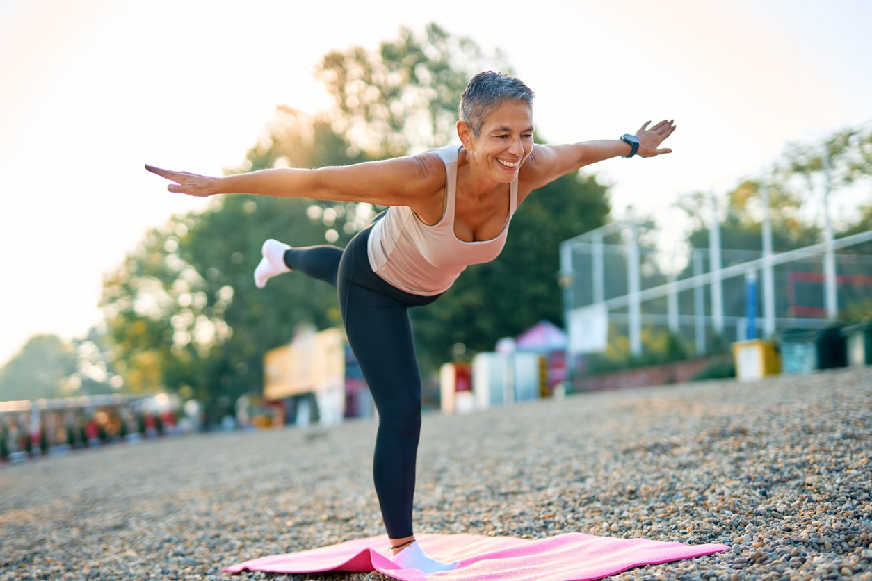 Woman practicing yoga outdoors, standing on one foot.